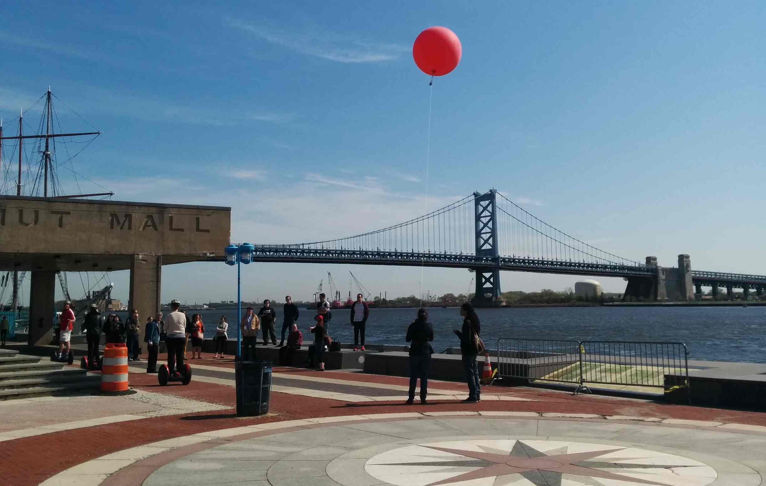 Image of red balloon floating above Ben Franklin Bridge, tethered