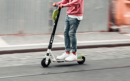 Man in sweater riding electric scooter through streets.